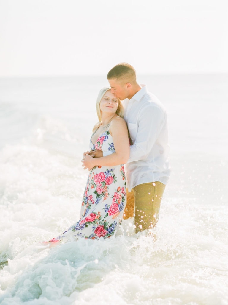 intimate couples pose at the beach as the waves crash around them