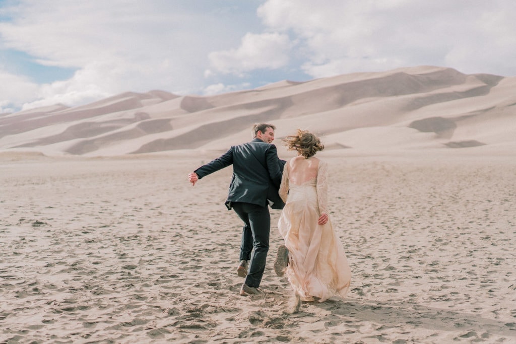 bride and groom runs towards the Great Sand Dunes of Colorado