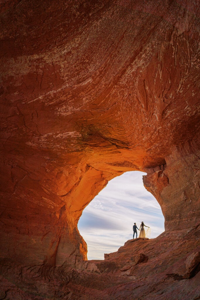 Couple standing together under a natural red rock arch in Moab, Utah.