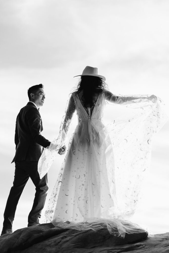 Black and white photo of a bride and groom standing on a rock in Utah.