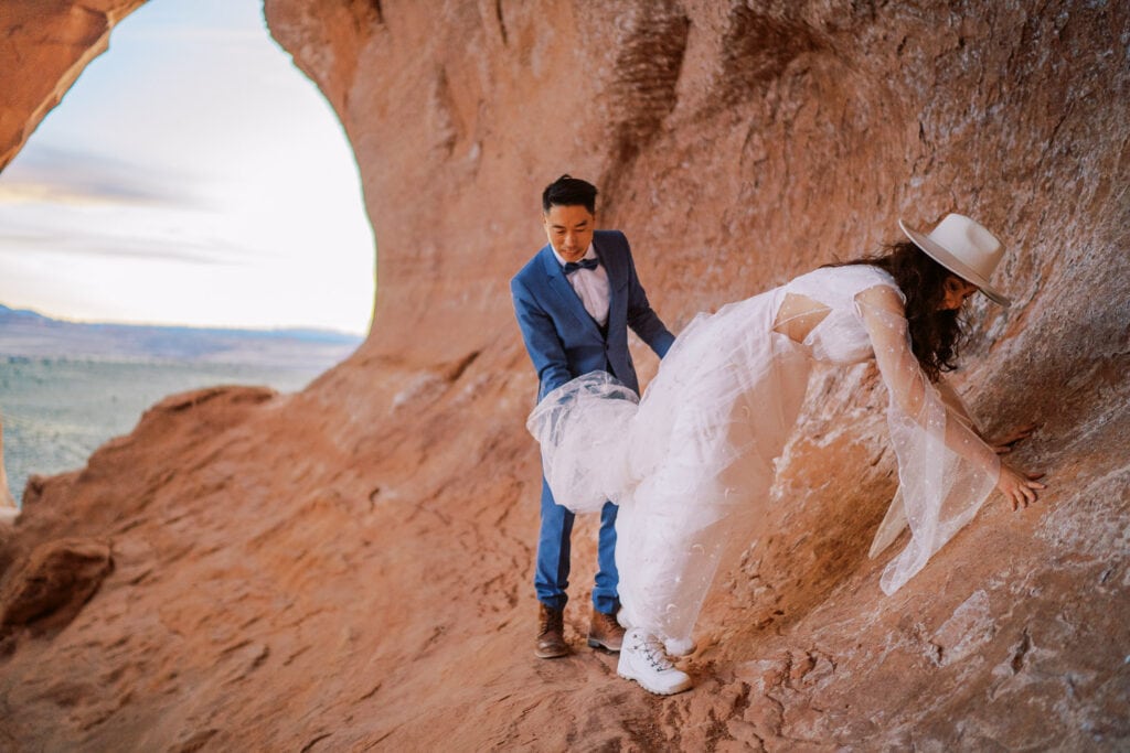 Bride and groom scrambling across red rocks in Moab during their wedding day.