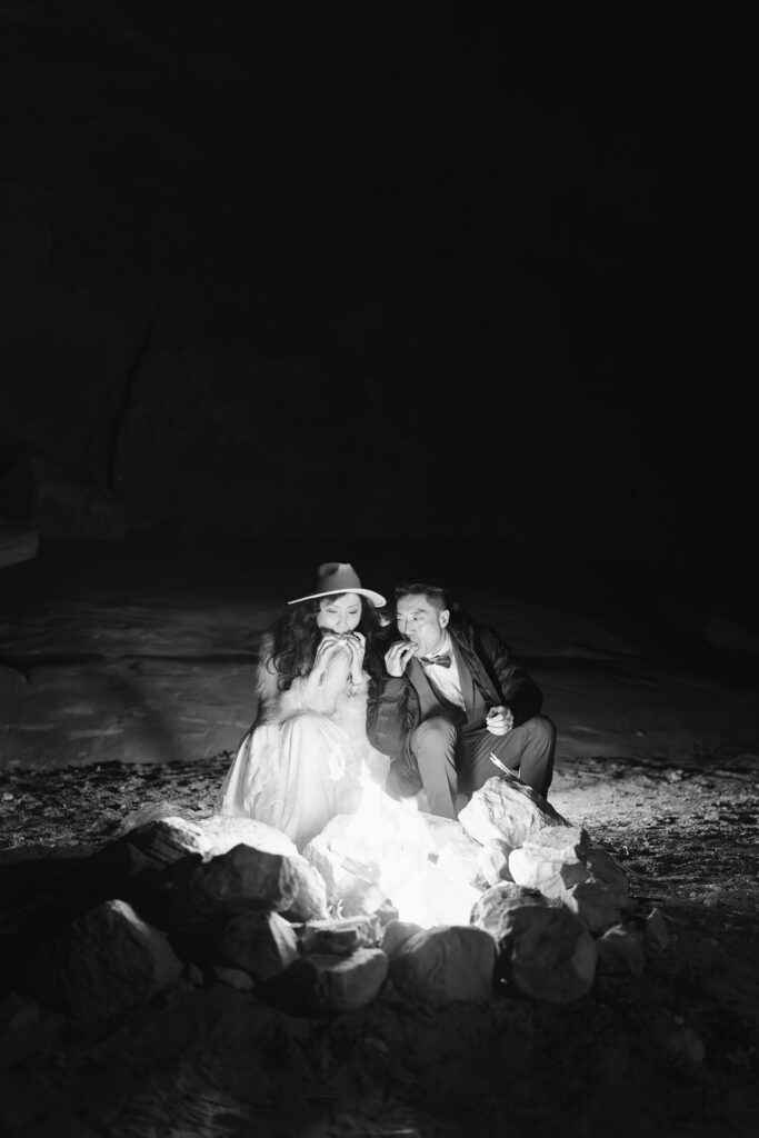 Bride and groom eating s'mores together by a campfire after their elopement day in Moab, Utah.