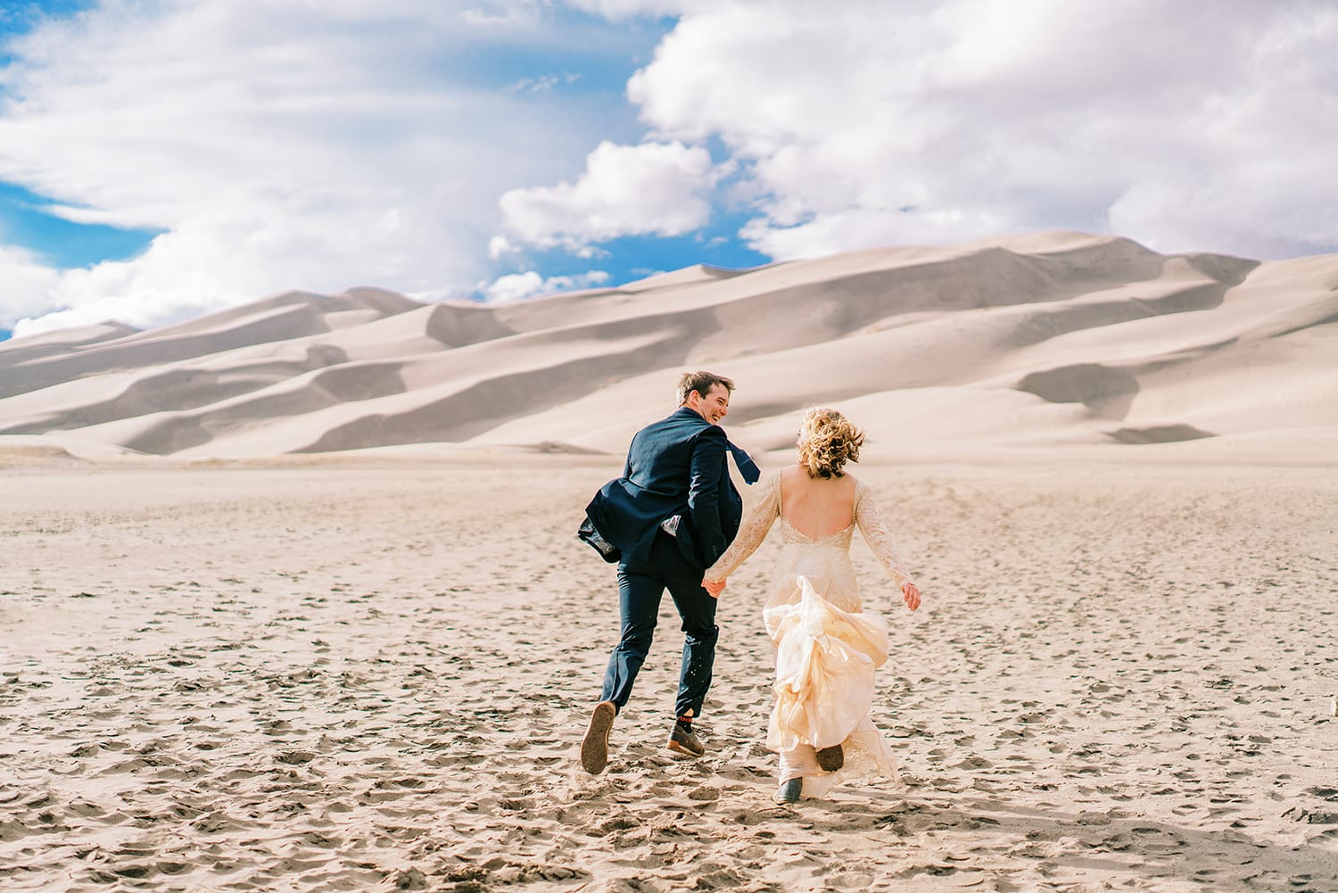 Bride and groom running in the sand in Great Sand Dunes National Park in Colorado.