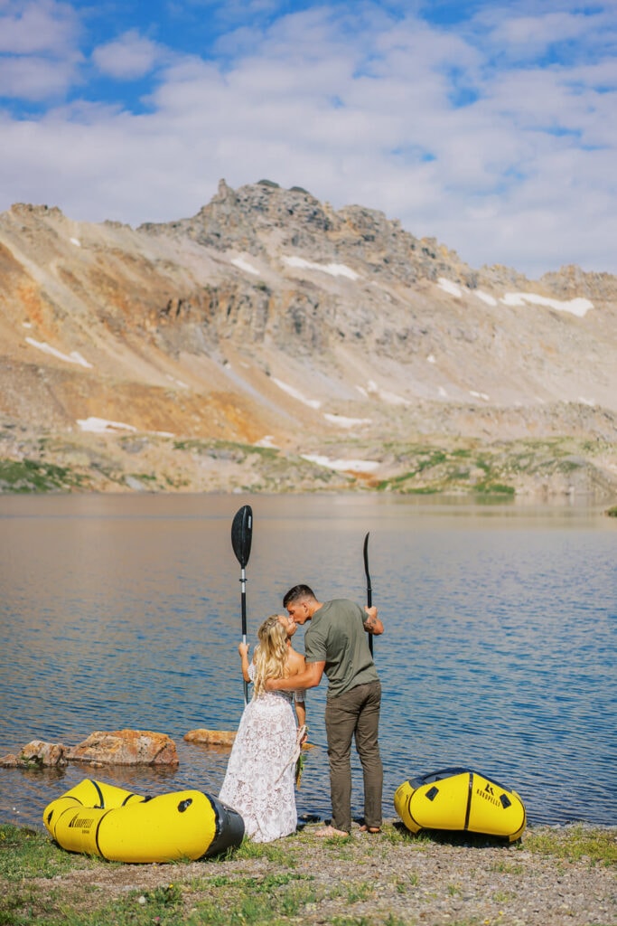 Bride and groom kiss just before pack rafting on an alpine lake in Colorado.