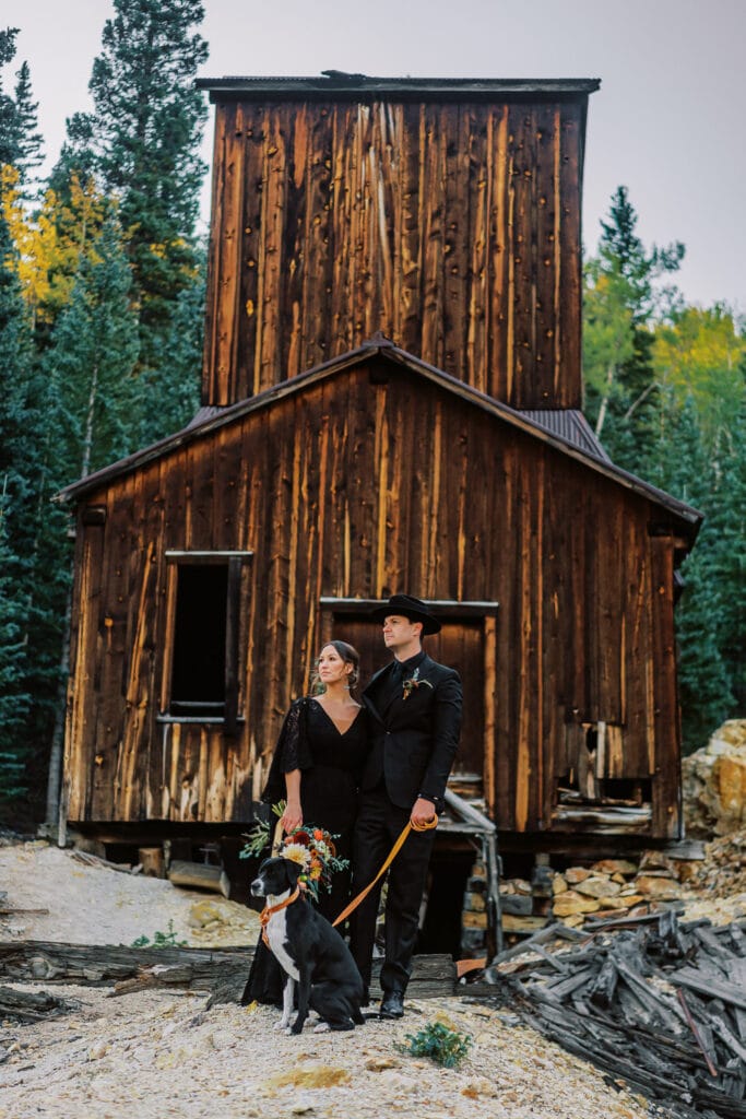 Bride and groom in all black in front of a historic mine in western Colorado for their elopement in the mountains.
