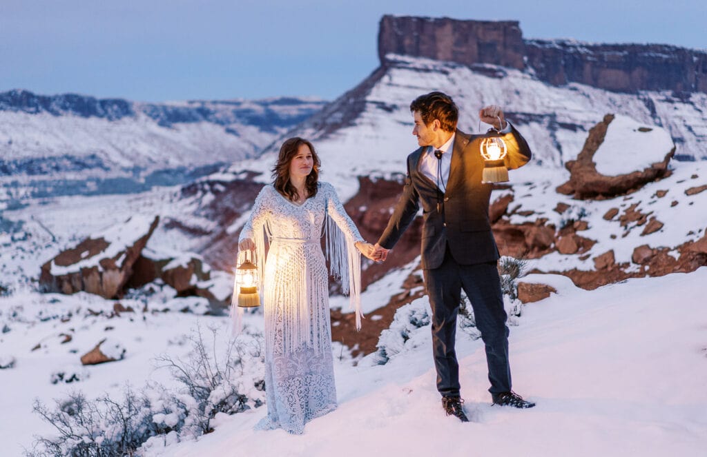 Bride and groom hiking in the snow in Moab with lanterns.