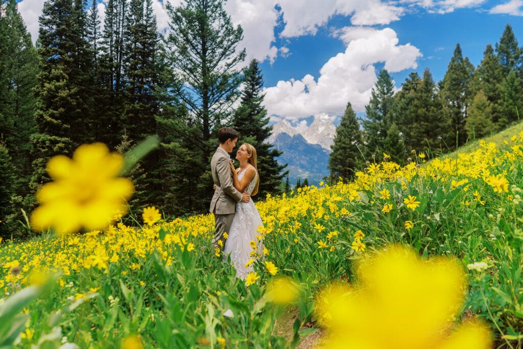 Bride and groom are surrounded by a field of yellow wildflowers in the Grand Tetons during their wedding day hike.