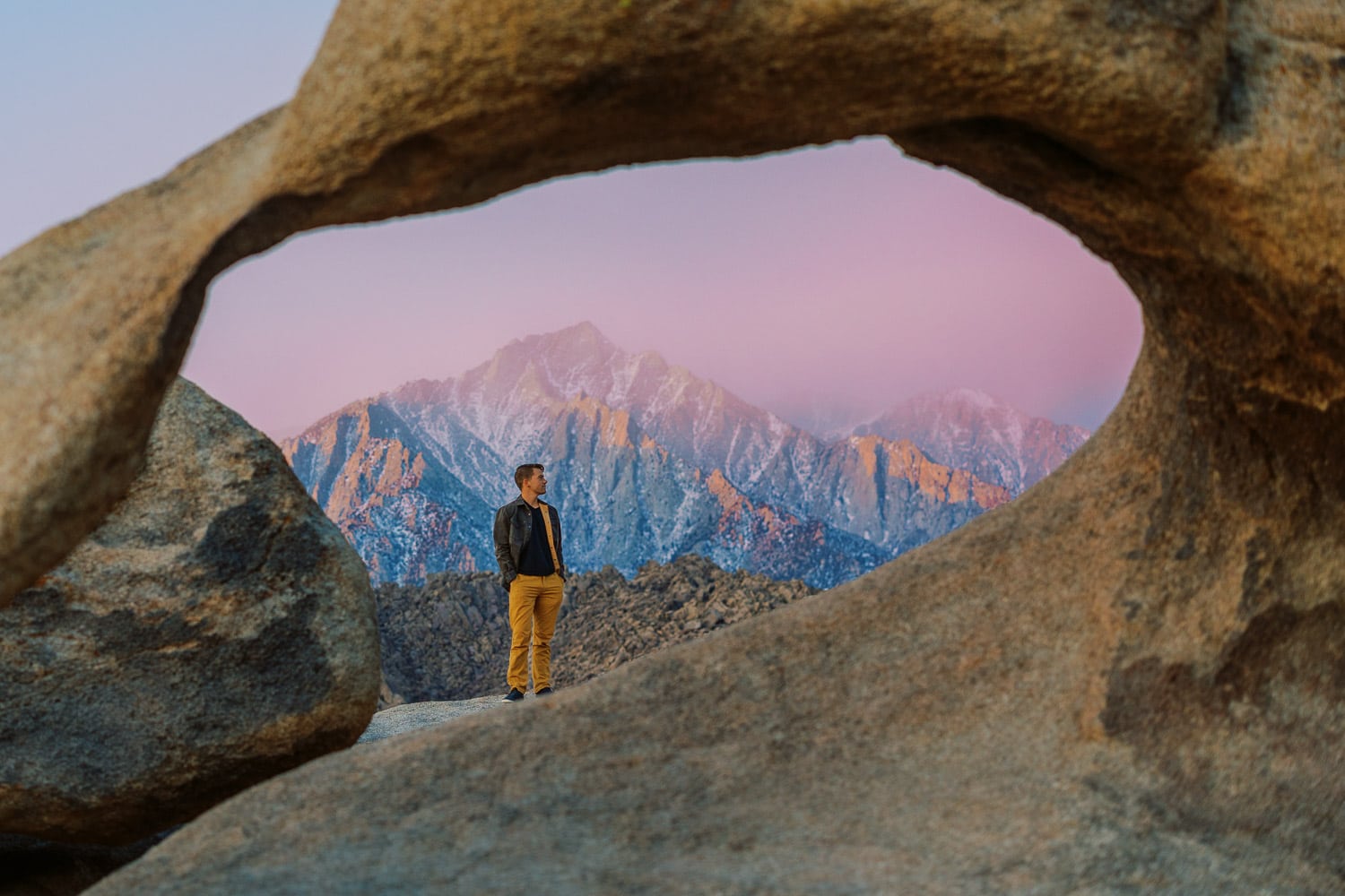 Malachi Lewis- a California elopepement photographer standing under an arch in Alabama Hills at sunrise.