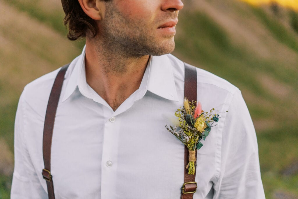 Groom with a boho style boutonniere and leather suspenders.