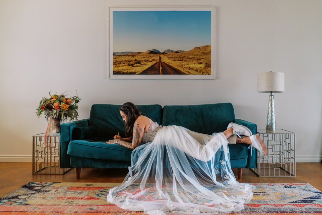 Bride in a jump suit writes her vows on a colorful couch before her hiking wedding day.