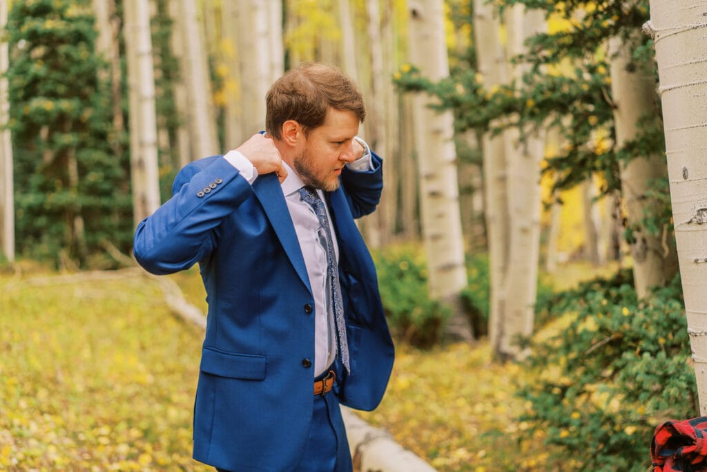 Groom gets ready out in the aspen trees and puts his suit jacket on.
