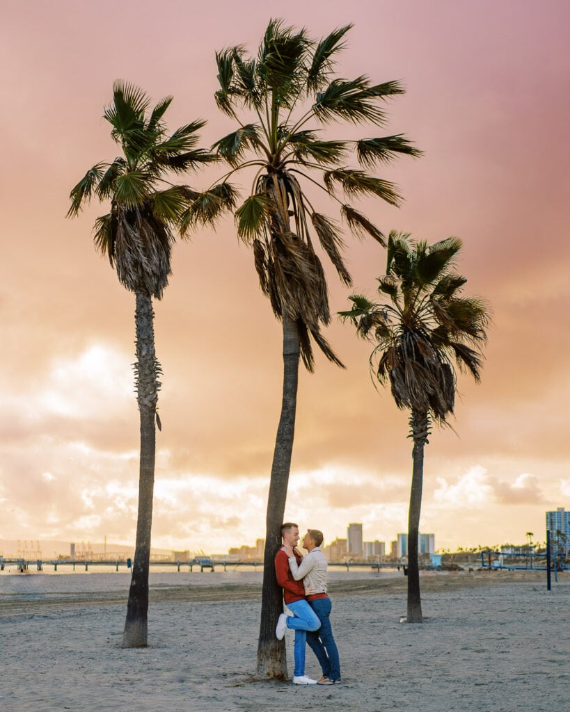 Two guys embrace under palm trees in California during a same sex gay engagement session.