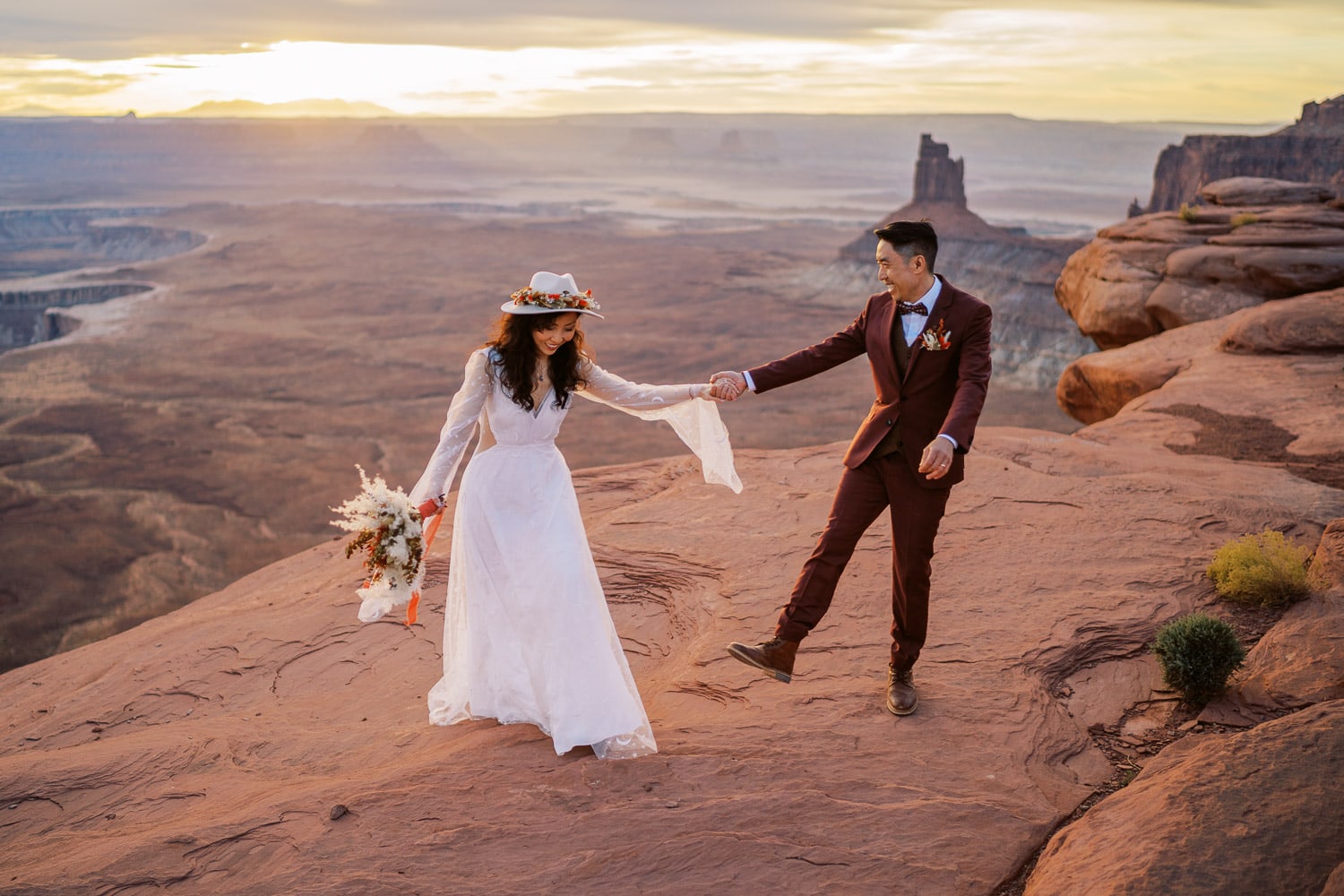 Adventure Elopement in Moab, Utah with a bride and groom dancing near a cliff at sunrise.