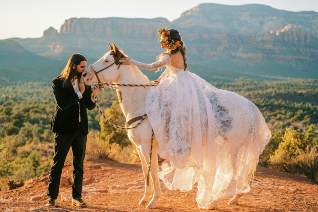 Bride rides a horse during their elopement in Sedona, Arizona while the groom kisses the horse on the nose.